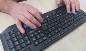 dłonie mężczyzny na klawiaturze komputerowej koloru czarnego położone na jasnym stoliku