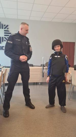 uczeń w hełmie i kamizelce kuloodpornej stojący przy policjancie
