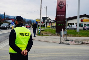 policjant stojący tyłem  spoglądający na drogę która poruszają sie samochody na tle szyldu Fabios