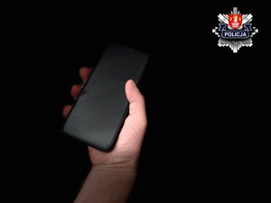 dłoń męska trzymająca telefon na czarnym tle a w prawym rogu gwiazda suskiej komendy