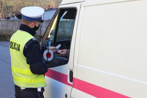 Umundurowany policjant z ruchu drogowego trzymający tarcze sygnalizacyjną w trakcie kontroli zabiera dokument prawa jazdy kierowcy