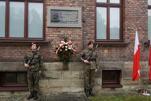 tablica Józefa Piłsudskiego wraz z kwiatami oraz wartą wojskową przy której znajduje się stojak z flagami polski