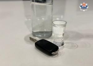 napełniony kieliszek którego tłem jest pełna butelka a obok kluczyki od samochodu na białym stole