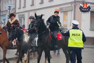 policjant ruchu drogowego w białej czapce wręcza odblaski osobą jadącym na koniach w czasie pochodu