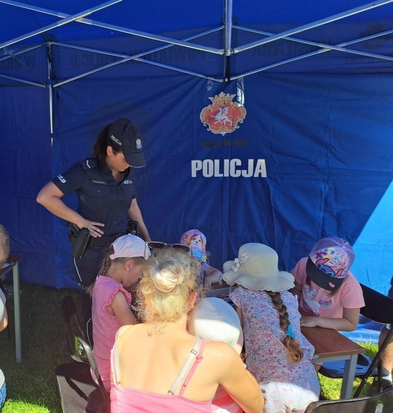policjantka stojąca przy dzieciak rysujących obrazki w namiocie profilaktycznym