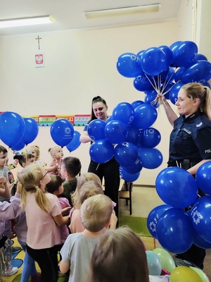 dzielnicowa i pracownik policji trzymająca duża ilość balonów które wręczają wszystkim małym słuchaczom