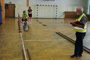 chłopiec na rowerze podczas pokonywania toru na hali w czasie turnieju i stojący obok niego sędzia