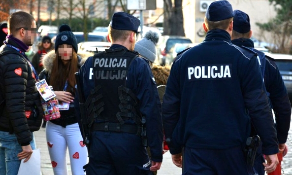 Zdjęcie przedstawiające patrol umundurowanych policjantów idących obok grupy młodzieży posiadającej obklejoną odzież w czerwone serduszka wielkiej orkiestry oraz młodego chłopaka trzymającego puszkę oraz posiadającego identyfikator na szyi wielkiej orkiestry świątecznej pomocy