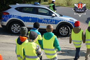 idące w kamizelkach odblaskowych dzieci na tle policyjnego radiowozu