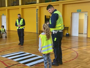 dziewczynka wraz z policjantem prezentują bezpieczne przechodzenie przez jezdnię