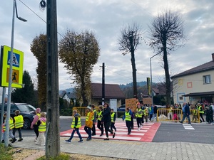 dzieci w ramach akcji odblaski przechodzą na przejściu dla pieszych w obecności policjantów w dalszą drogę wzdłuż drogi wojewódzkiej