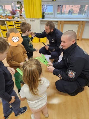 dzielnicowy wręczają przedszkolakom opaski odblaskowe