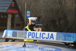 policjant ruchu drogowego mierzący prędkość kierowcą na tle napisu Policja z sygnałami świetlnymi zamieszczonego na dachu oznakowanego radiowozu