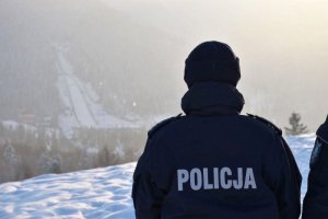 policjant stojący tyłem na tle wyciągów narciarskich