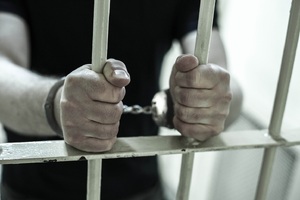 ręce zatrzymanego z kajdankami trzymające kratę policyjnej celi