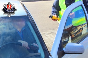 siedzący kierowca i policjant ruchu drogowego z trzymającym urządzeniem do badania trzeźwości