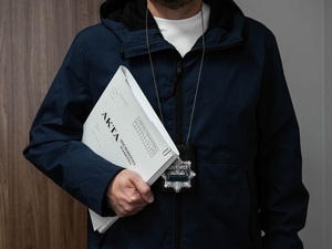 policjant kryminalny z zawieszoną odznaką na szyi trzymający teczkę z aktami