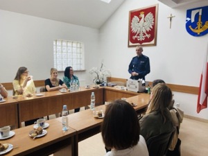 Policjant podczas spotkania omawiający temat i położoną przed nim walizka profilaktyczną