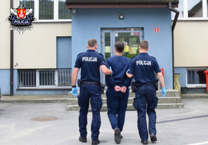 zatrzymany idący w obecności policjantów z założonymi kajdankami na rękach z tyłu