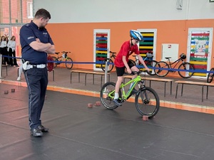 policjant ruchu drogowego przyglądający się uczniowi na rowerze podczas zadania z umiejętności jazdy na rowerze
