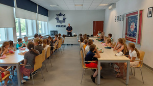 Dzieci siedzące w sali audiowizualnej i słuchające wykładu policjanta na temat bezpieczeństwa
