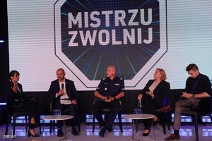 Uczestnicy inauguracji kampanii siedzą na krzesłach ustawionych na scenie. W tle na ekranie wyświetlany slajd z logiem Mistrzu zwolnij.