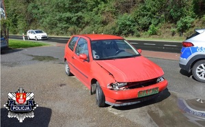 uszkodzony czerwony volkswagen i stojące obok drogi oznakowane radiowozy