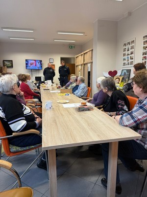 Dzielnicowi tłumaczący na temat bezpieczeństwa seniorom siedzacym przy stole