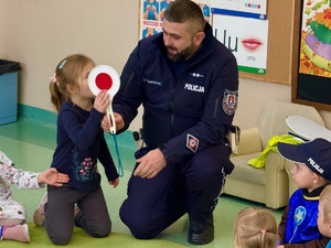 Policjnat prezentujący tarczę sygalizacyjną przedszkolakom
