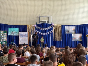 Policjant z chłopczykiem stojący przed zgromadoznymi na hali dziećmi