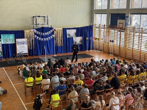 Ujecie z góry policjanta i siedzących na hali dzieci w czasie zajęć edukacyjnych