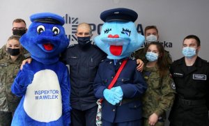 Komendant Wojewódzki stojący z maskotkami smokiem i smoczycą w stroju policyjnym wraz z uczniami klas mundurowych