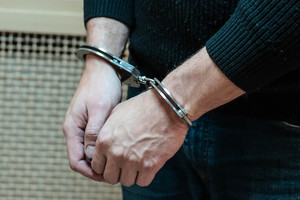 dłonie mężczyzny w ciemnym swetrze z założonymi kajdankami