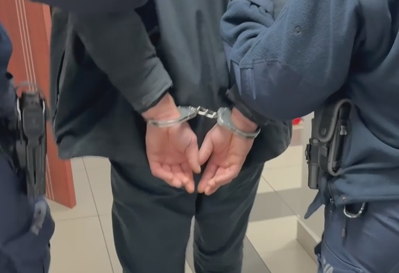 mężczyzna prowadzony przez policjantów w kajdankach