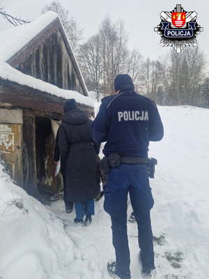 Policjant stojący z pracownicami gops przed malutkim domkiem pokrytym grubą warstwą śniegu