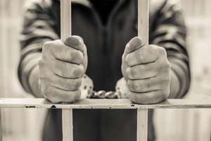 osoba zatrzymana w kajdankach trzymająca celną kratę