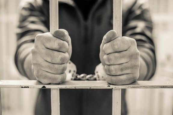 osoba zatrzymana w kajdankach trzymająca celną kratę