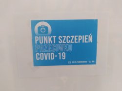 Zdjęcie przedstawiające tabliczkę na ścianie koloru niebieskiego z białym napisem punkt szczepień przeciwko covid 19