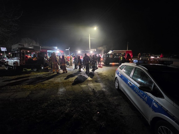 policyjny radiowóz a w tle służby biorące udział w poszukiwaniach