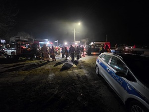 policyjny radiowóz a w tle służby biorące udział w poszukiwaniach