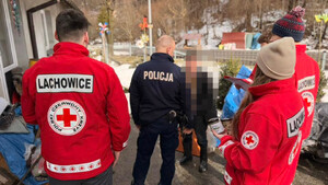 Dzielnicowy rozmawia z seniorem a zanim stojący wolontariusze pck