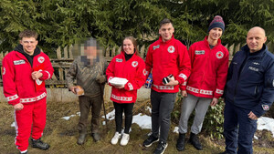 Pozujący do zdjęcia dzielnicowy wraz z wolontariuszami i seniorem w czasie przekazania posiłku