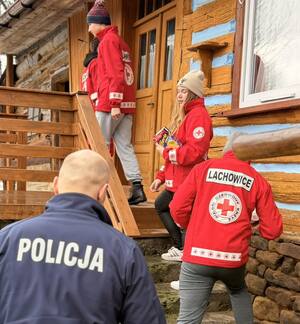 Dzielnicowy wraz z wolontariuszami wchodzi do drewnianego domku