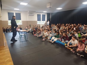 Policjant z wydziału ruchu drogowego stojący przed grupą dzieci w czasie zajęć