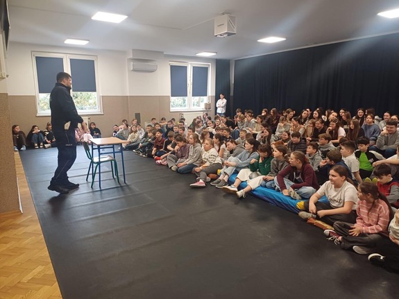 Policjant z wydziału ruchu drogowego stojący przed grupą dzieci w czasie zajęć