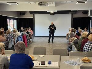 Dzielnicowy z mikrofonem i słuchające go seniorki