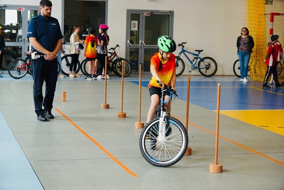 uczeń na rowerze podczas turnieju brd wykonuje zadanie w obecności stojącego obok policjanta