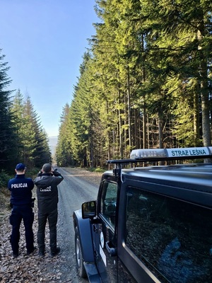 Dzielnicowy ze strażnikiem leśnym stojący przy jeepie