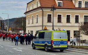 policyjny radiowóz a przed nim policjanci i idąca grupa kibiców w kierunku ulicy zamkowej w suchej beskidzkiej