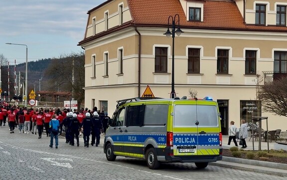 policyjny radiowóz a przed nim policjanci i idąca grupa kibiców w kierunku ulicy zamkowej w suchej beskidzkiej